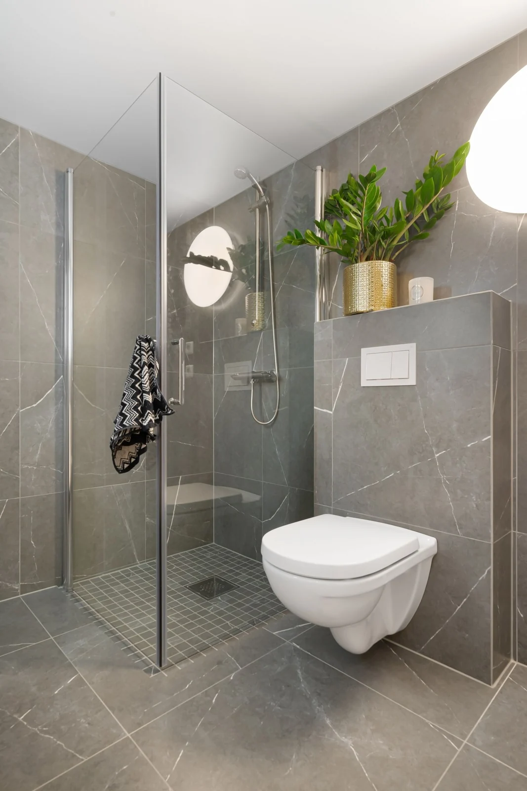 Contemporary bathroom featuring gray tiles, glass shower, and toilet with indoor plant