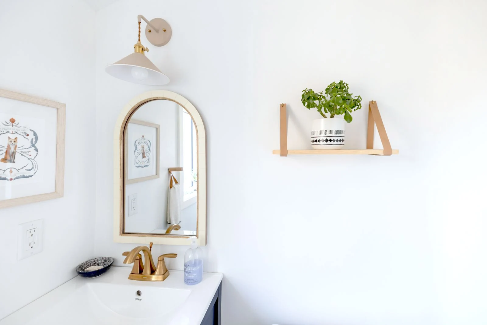 Bright and simple bathroom interior with a gold-framed mirror and decorative shelf