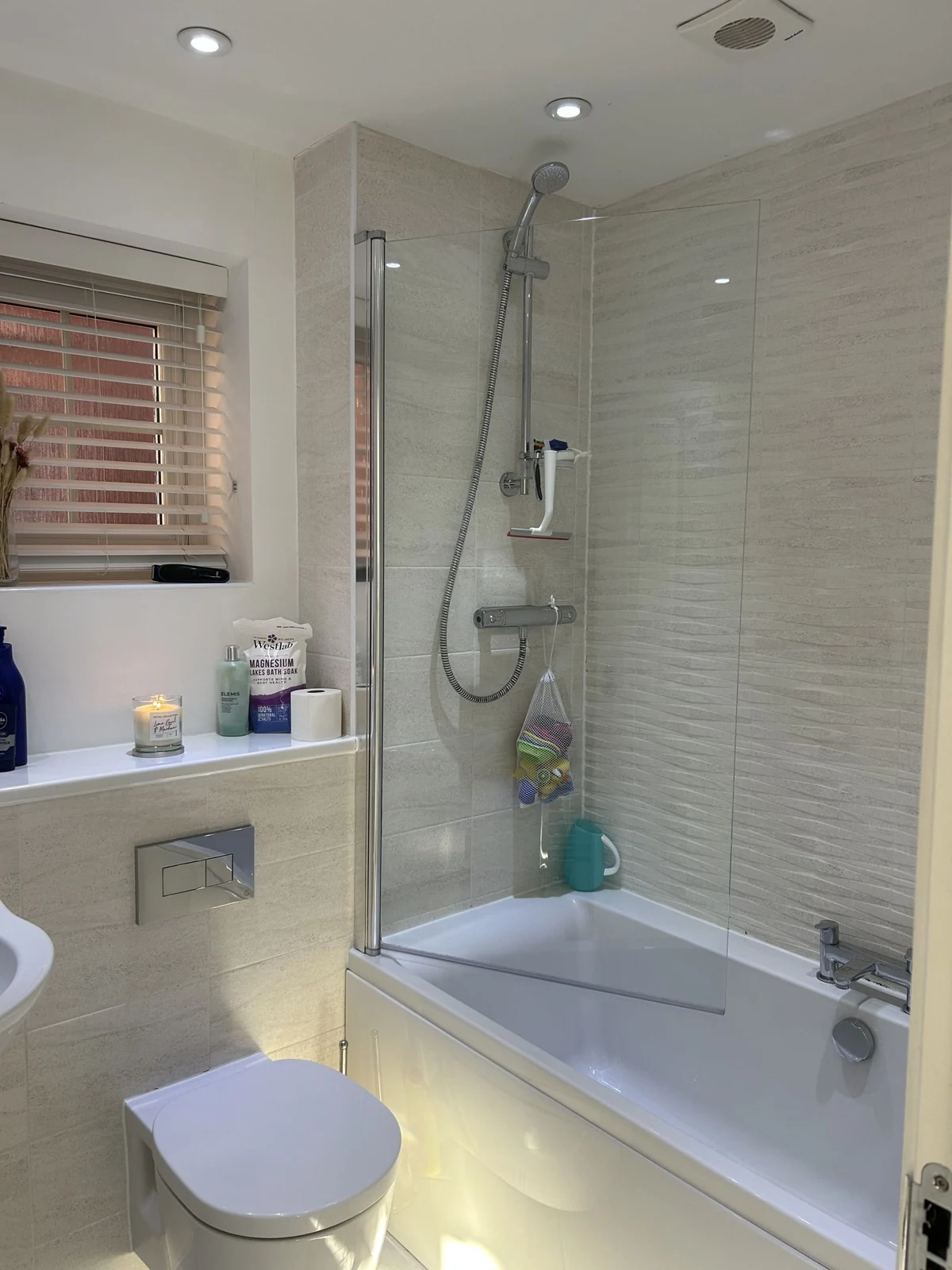 Bright modern bathroom featuring a bathtub with shower, toilet, and natural light