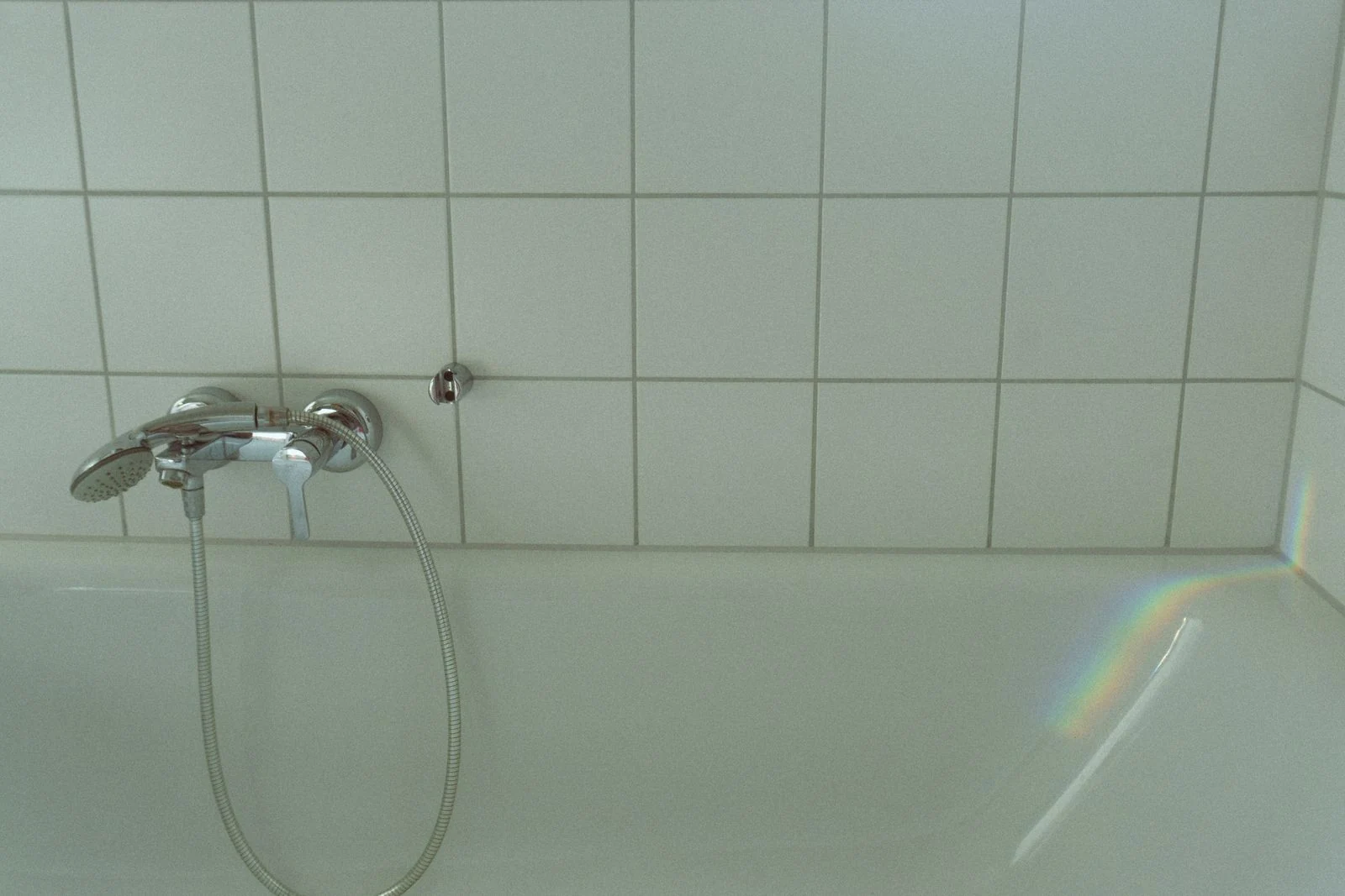 A modern bathroom interior featuring a white bathtub and a gentle rainbow reflection on tiled walls