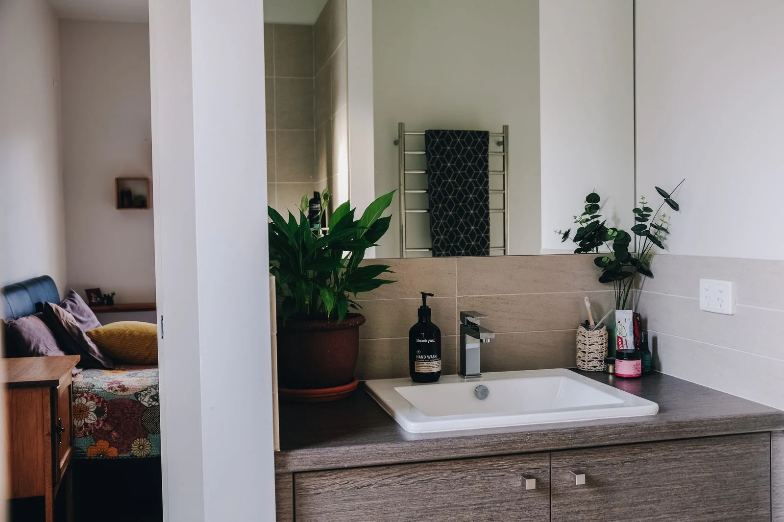 Interior of modern bathroom with mirror above white sink and wooden cabinet decorated with potted plants in apartment
