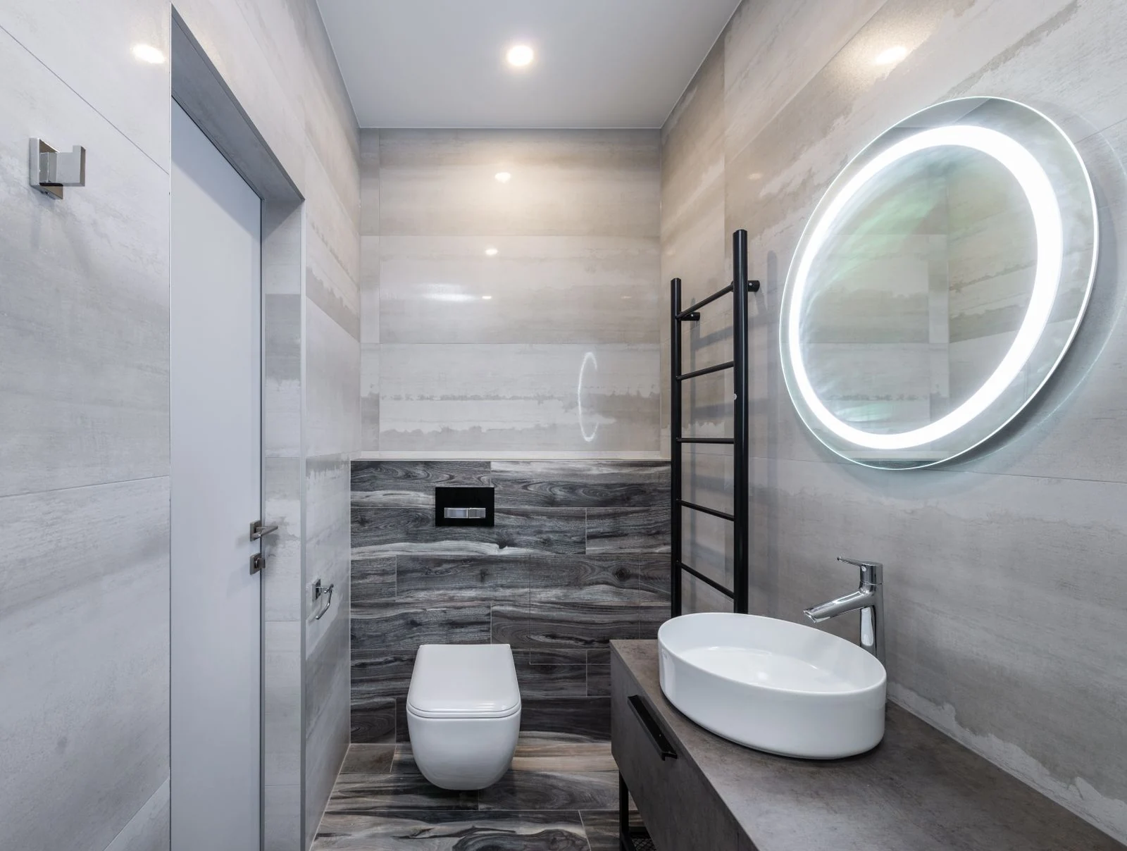 Contemporary bathroom with toilet bowl and washstand between cabinet and oval shaped mirror with glowing lamp