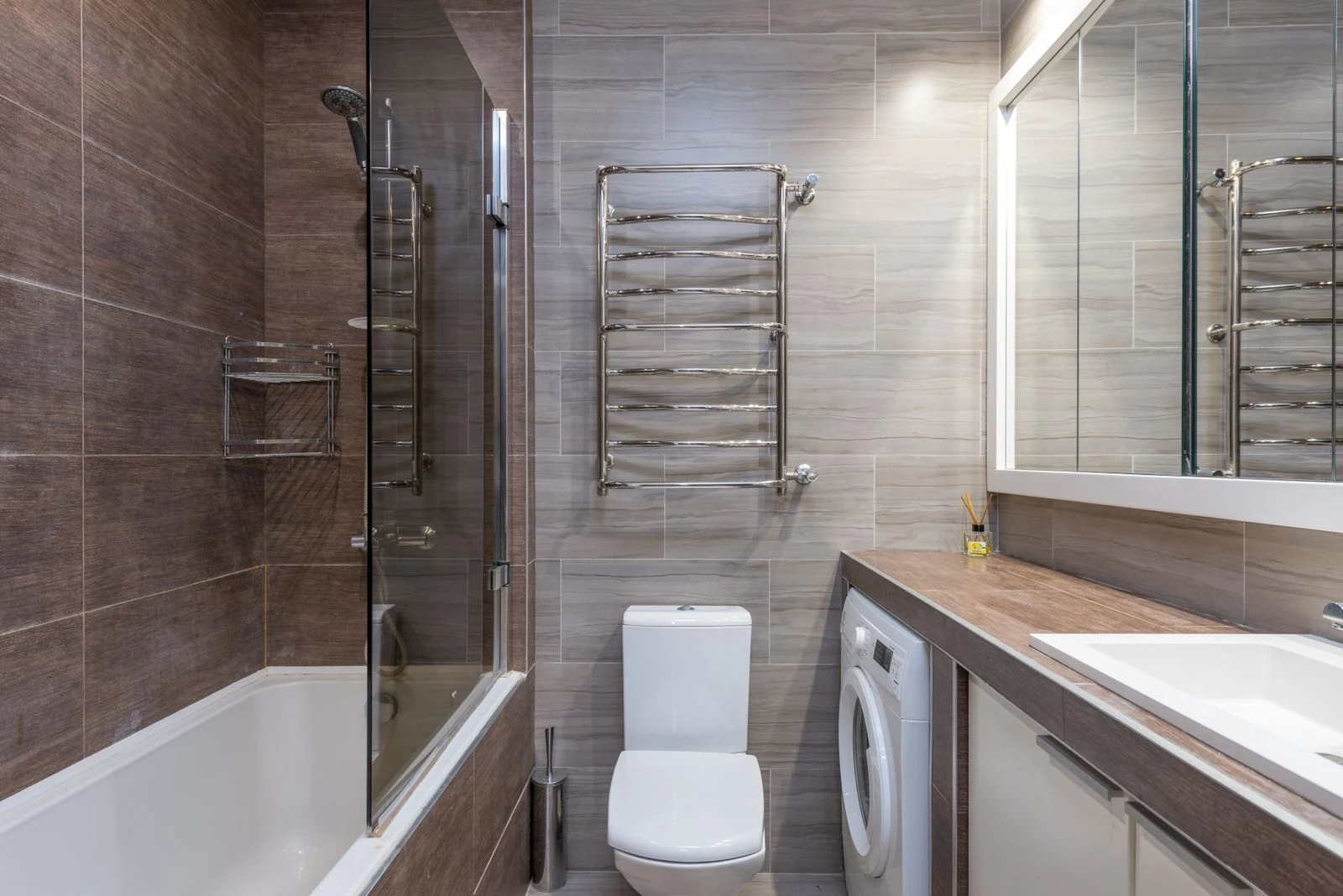 Interior of modern bathroom with bathtub toilet bowl and sink under big illuminated mirror