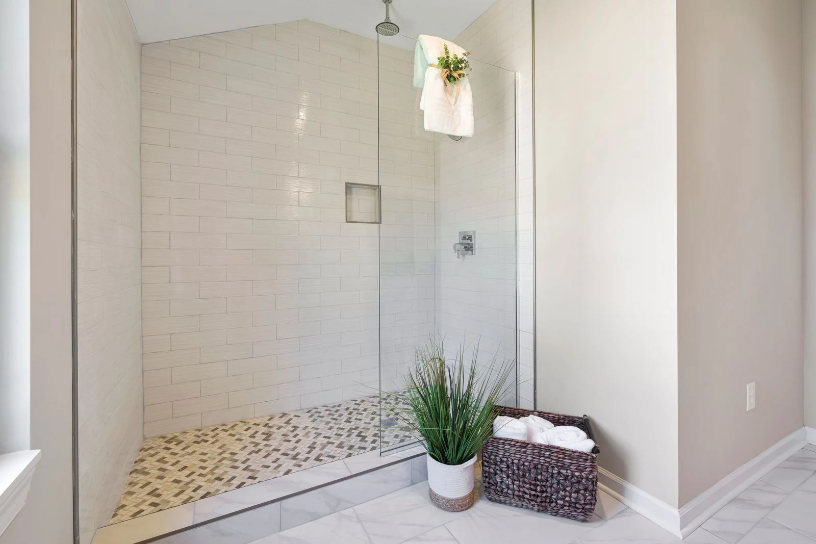 A minimalist bathroom featuring a sleek glass shower design with decorative plants and neatly arranged towels